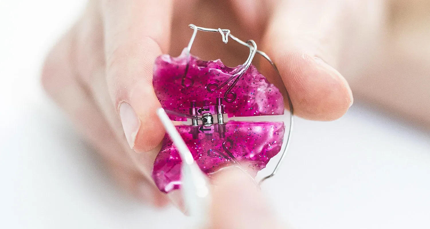 Rosa herausnehmbare Zahnspange wird in der Hand gehalten